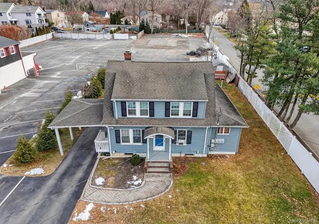Aerial view of a blue two-story house with a driveway and surrounding parking lot.