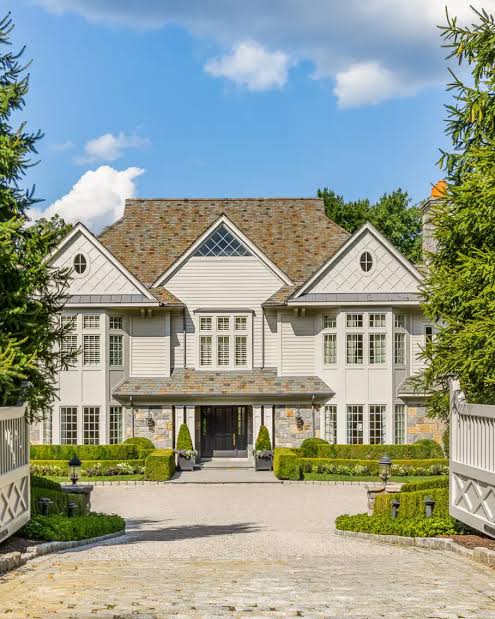 Greenwich real estate cream and stone luxury manor with slate roof, cobblestone driveway, manicured boxwood hedges, and white fence