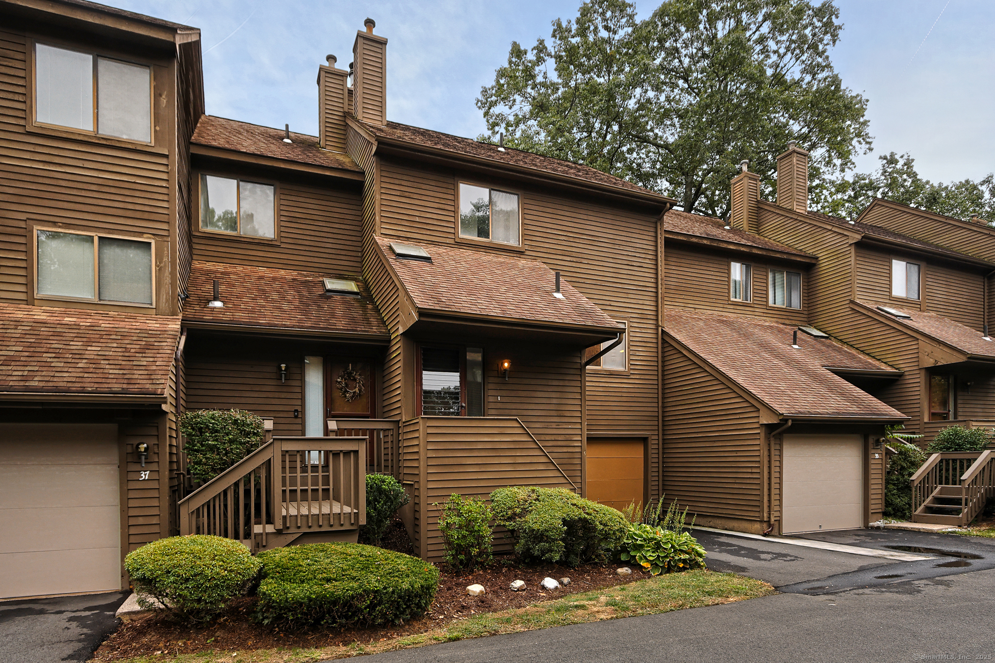 Hamden real estate brown wood-sided townhouse with multiple chimneys, attached garage, and landscaped shrub entryway