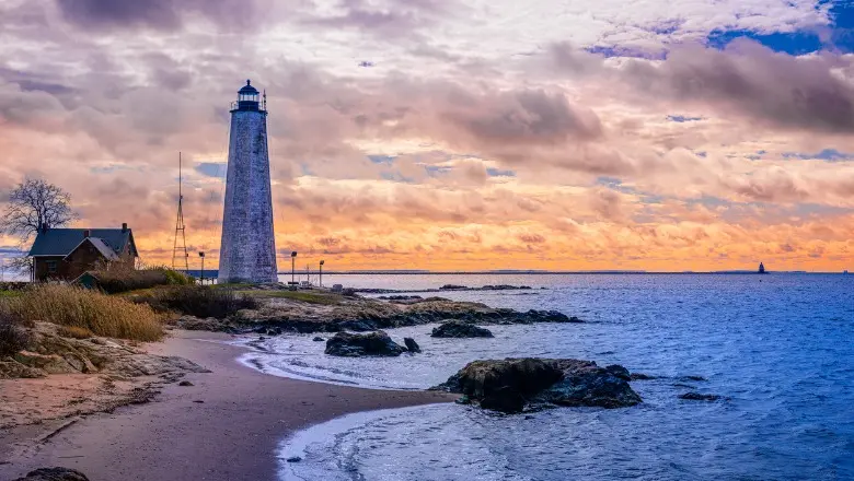 Lighthouse on rocky beach at sunset.