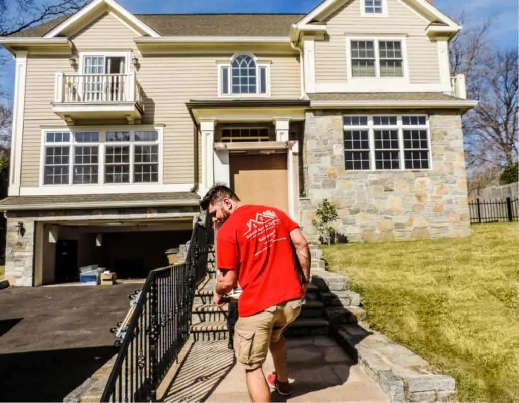 Man in red shirt walking up front steps of a suburban house during exterior home work.