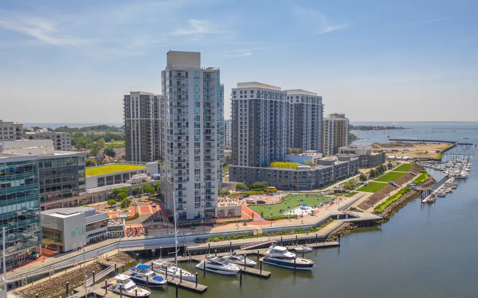 Modern waterfront development with high-rise residential buildings, marina, and public green space along the shoreline.