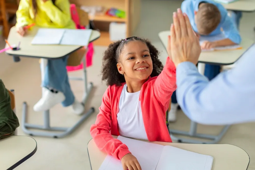 Student high-fiving teacher in a classroom.