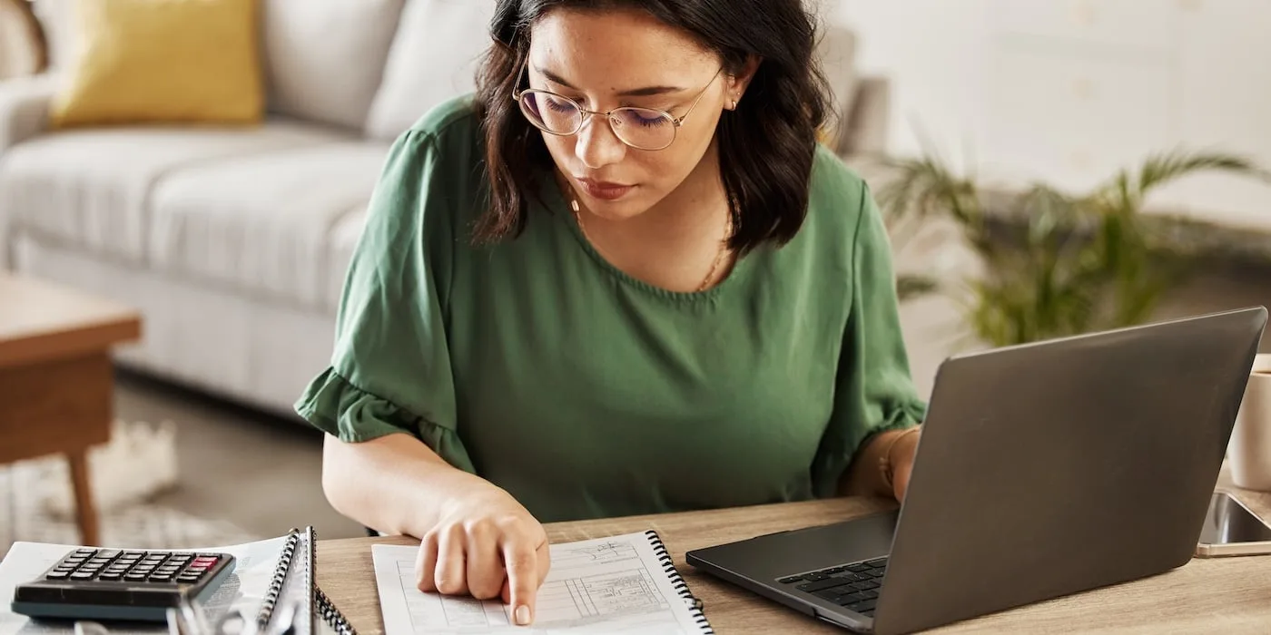 a lady calculating tax bill on a piece of paper, laptop open infront of her