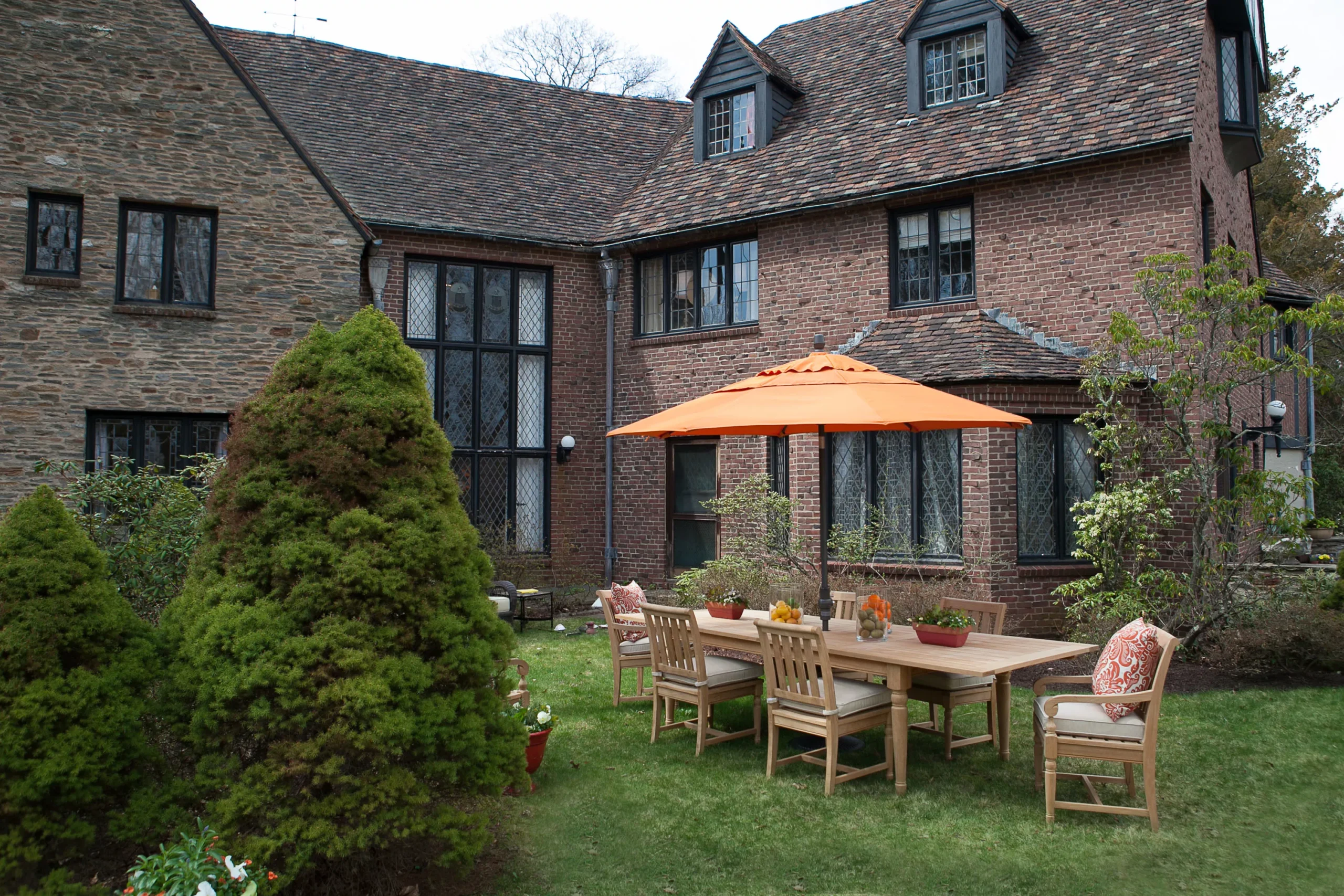 West Hartford real estate red brick Tudor home backyard with diamond windows, outdoor dining table, and orange patio umbrella